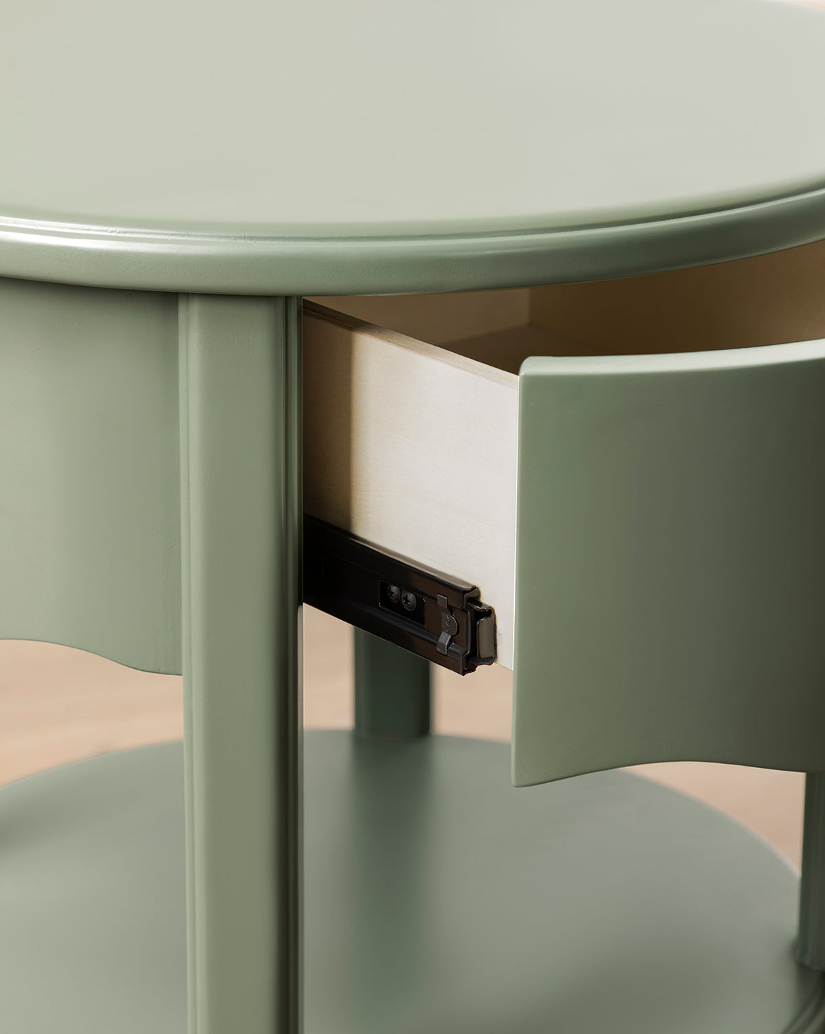 Close-up of the Liberty Nightstand, a round, light green piece with a glossy finish. Its small drawer is partially open, revealing the light wood interior and black metal sliding mechanism, by McGee & Co.