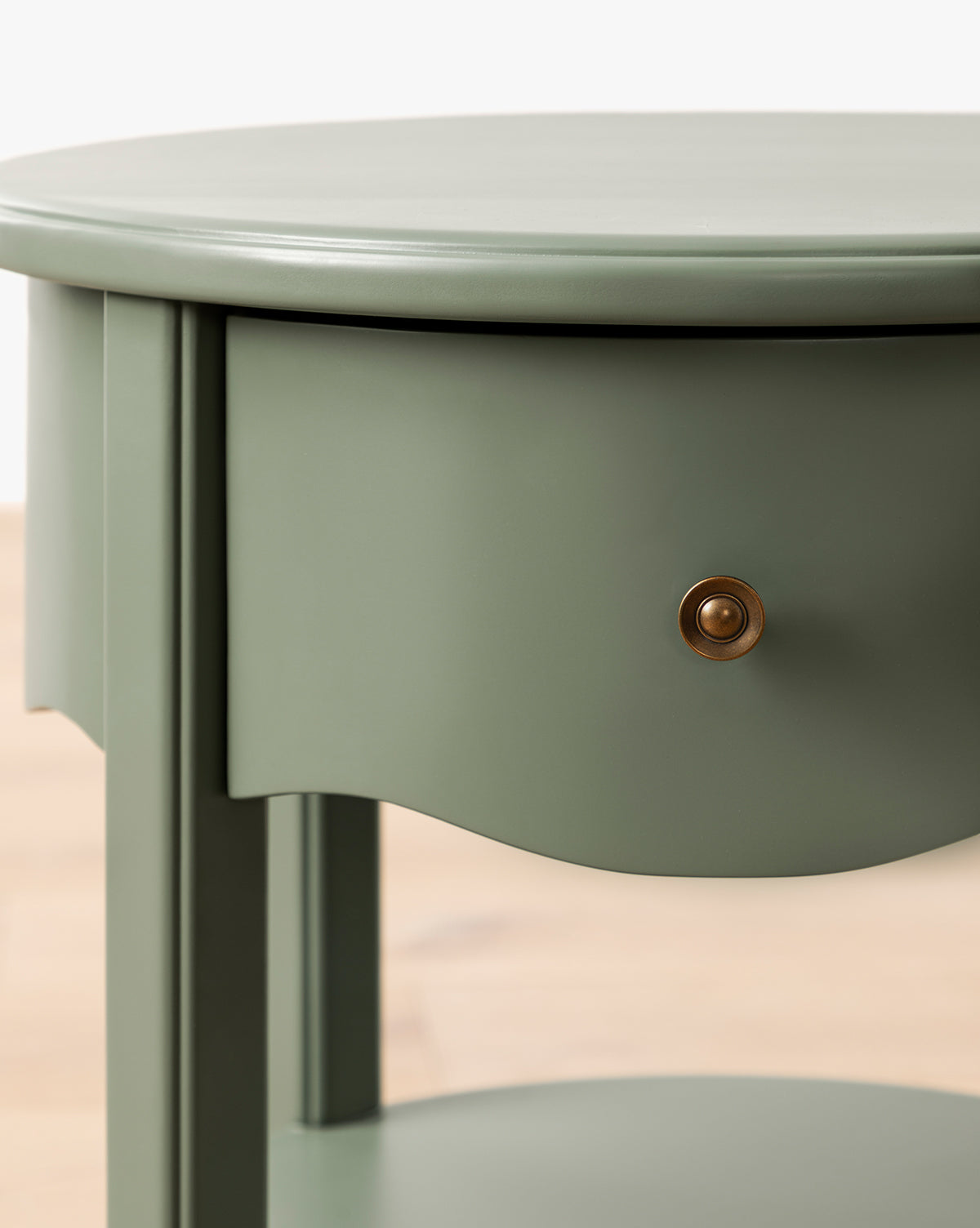 Close-up of the Liberty Nightstand—light green, round, with a single brass-knob drawer and open lower shelf on a light wood floor—perfect as a stylish GREENGUARD Gold Certified nursery nightstand by McGee & Co.
