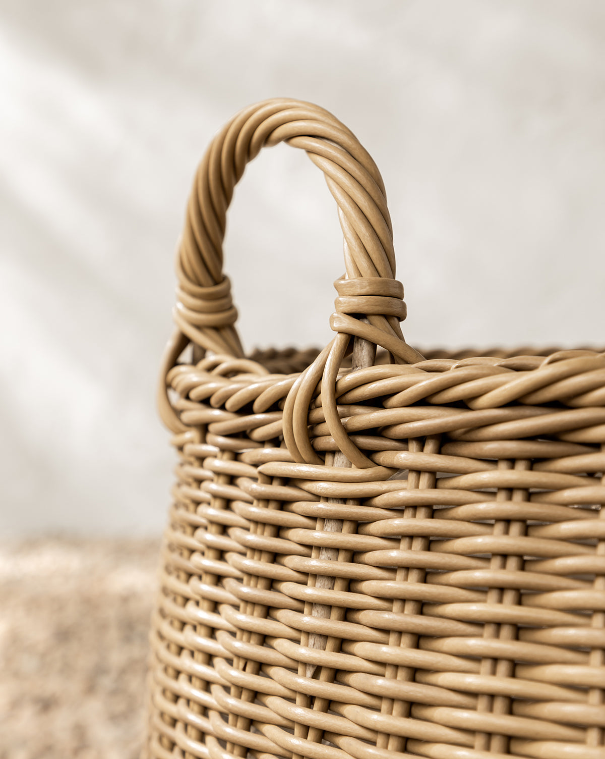 Close-up of the Lightwash Handled Planter Basket, featuring a sturdy, twisted poly-rattan handle and an intricate light tan weave—perfect for displaying indoor plants against a softly blurred neutral background, by McGee & Co.