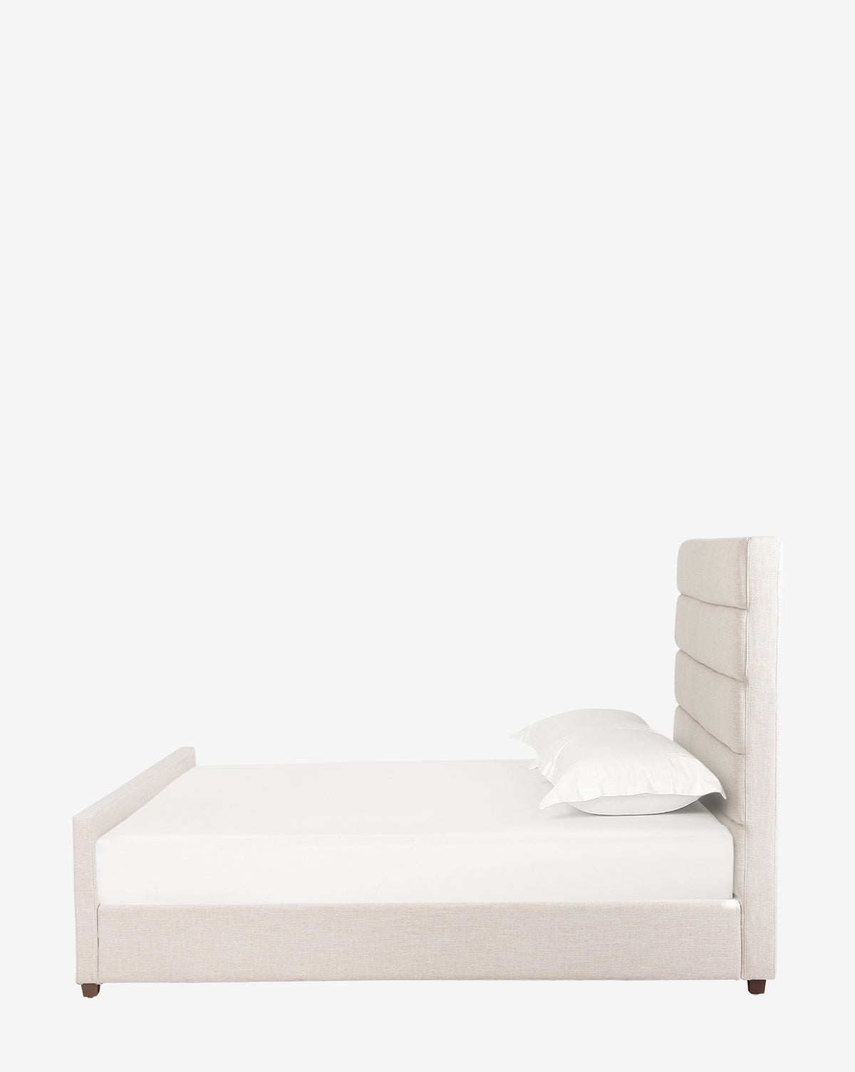 The Lila Bed showcases a modern design with a tall, padded rectangular headboard and low side rails upholstered in light beige fabric, paired with a white mattress and two white pillows for a sleek, contemporary look.