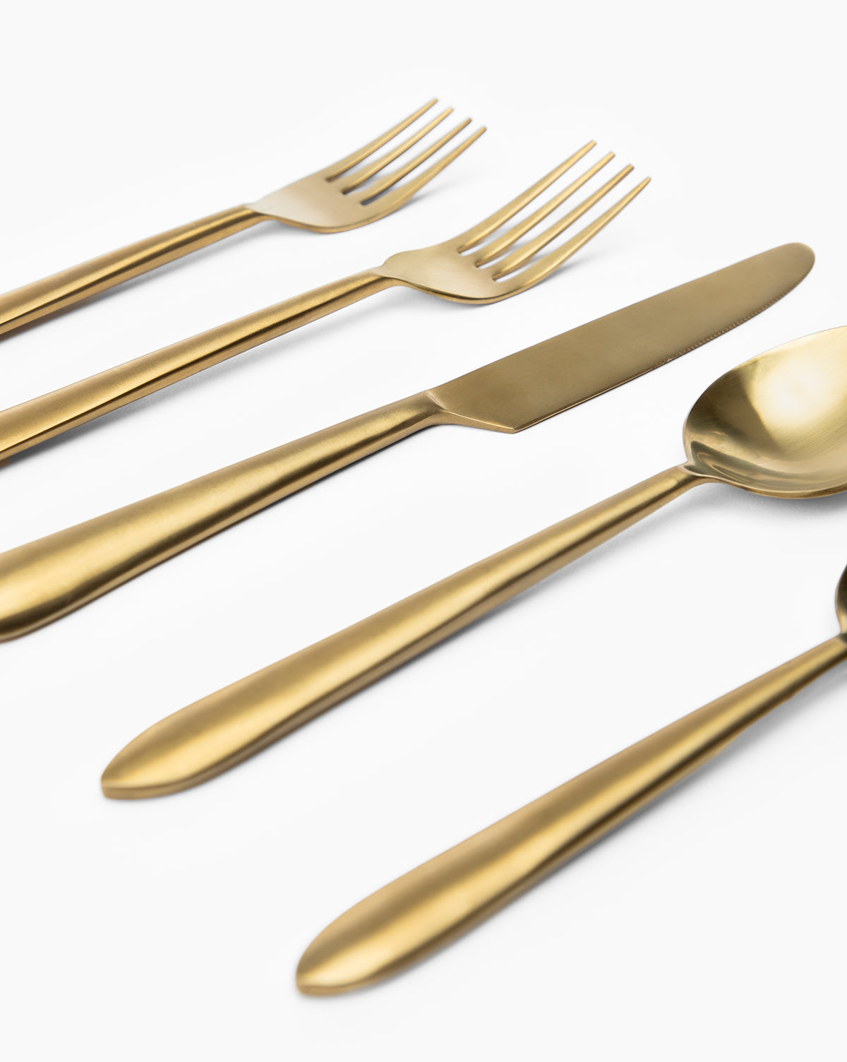 The Lilia Flatware (Set of 5), featuring gold-colored stainless steel utensils—two forks, a knife, a tablespoon, and a teaspoon—is arranged neatly on a white background.
