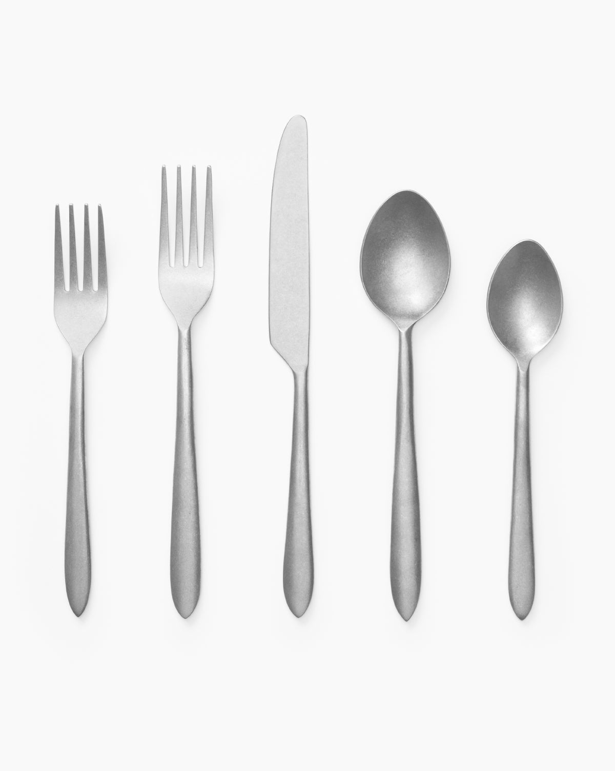 The Lilia Flatware (Set of 5)—two forks, a knife, a tablespoon, and a teaspoon—are arranged in a row on a white background.