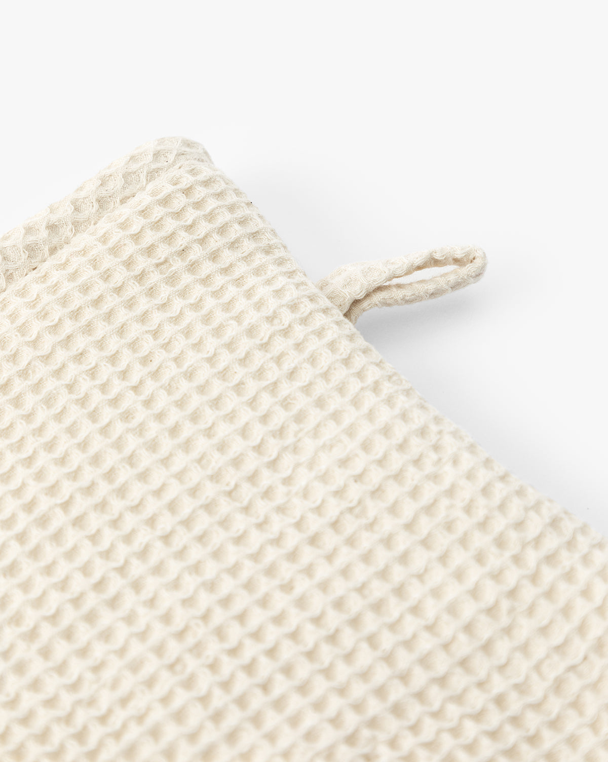 Close-up of a beige, textured waffle-knit fabric with a small loop on the edge—the Linen Blend Waffle Oven Mitt is a kitchen essential, shown against a white background, by McGee & Co.