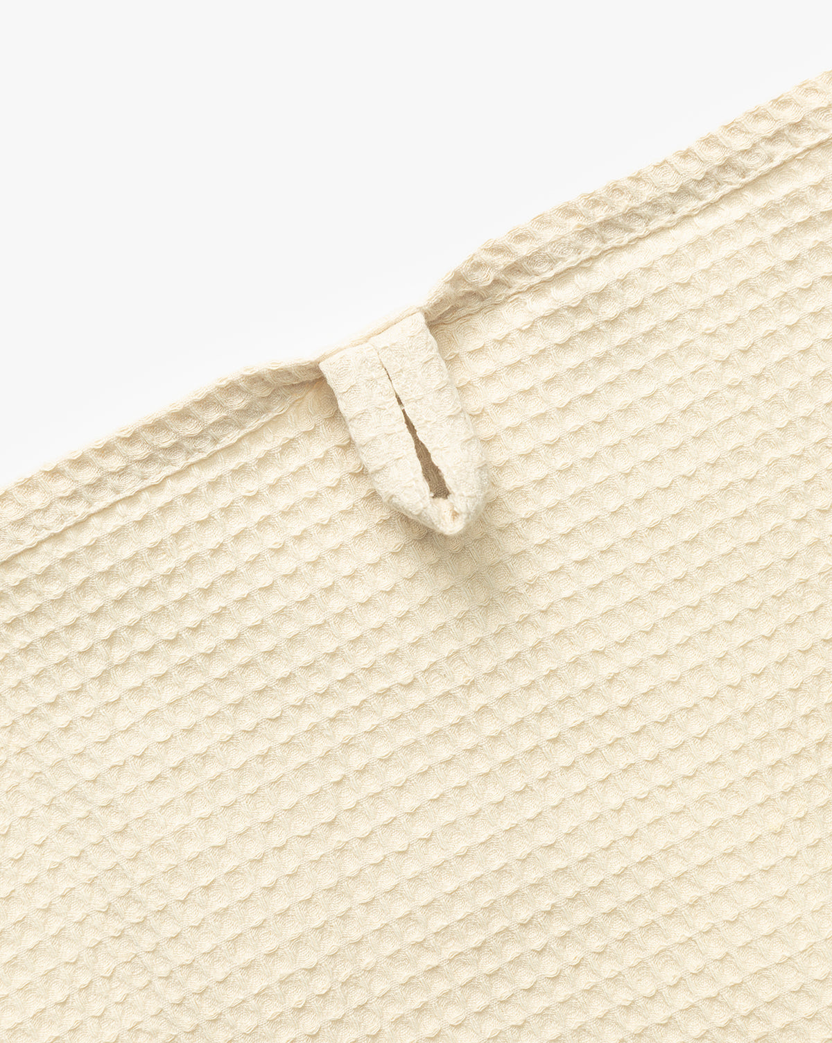 Close-up of the Linen Blend Waffle Tea Towel in beige, featuring a textured surface and a small hanging loop near the edge. This absorbent kitchen essential is shown flat on a white background, by McGee & Co.