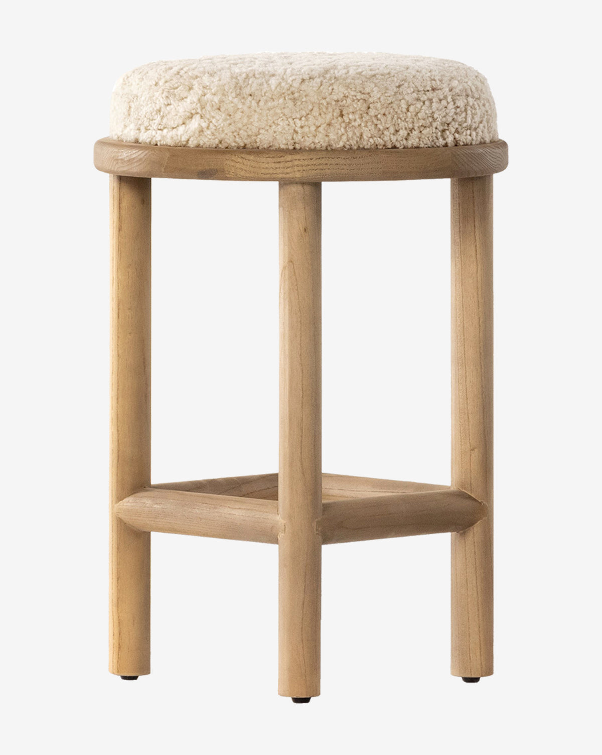 The Linus Stool is a three-legged wooden stool with a round, padded beige shearling seat, offering a simple, minimalist design ideal for counter seating, by McGee & Co.