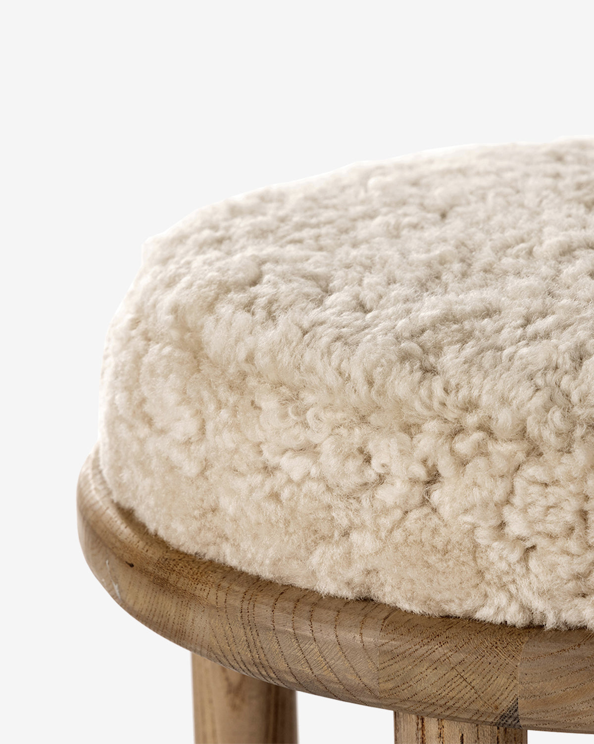 The Linus Stool features a round, plush beige shearling cushion on a smooth wooden base and legs—ideal for counter seating, by McGee & Co.