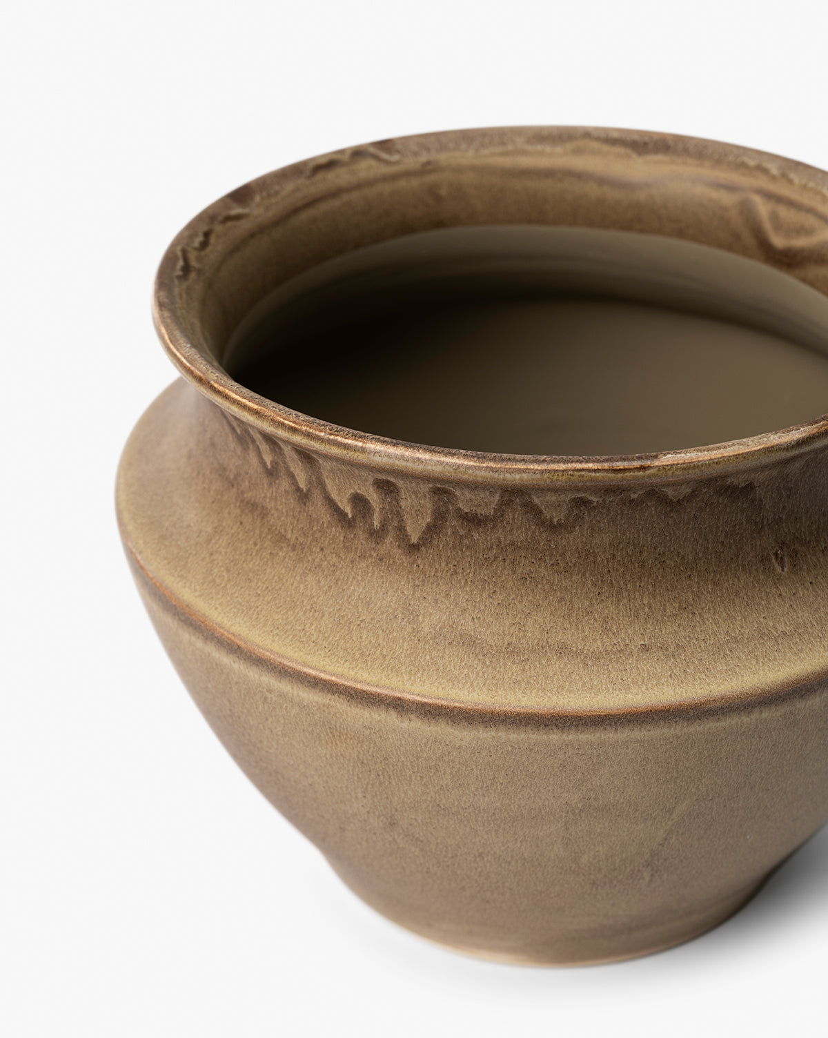 A close-up of the Liora Pot—a round, brown ceramic planter with a wide opening and natural glaze variations—ideal for adding style to your space, shown against a plain white background, by McGee & Co.