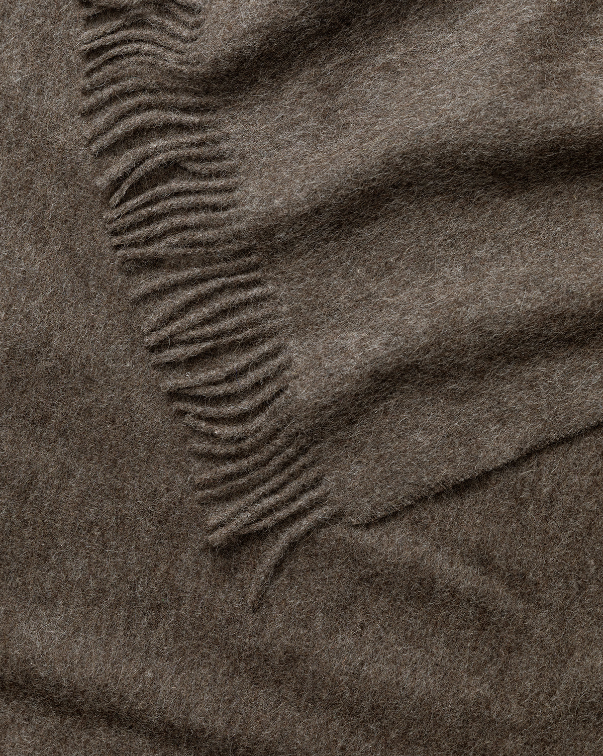 A close-up of the Fibre Locester Throw, crafted from soft brown wool with fringed edges and gentle folds, highlights the cozy, eco-friendly texture of this stylish home accessory by McGee & Co.