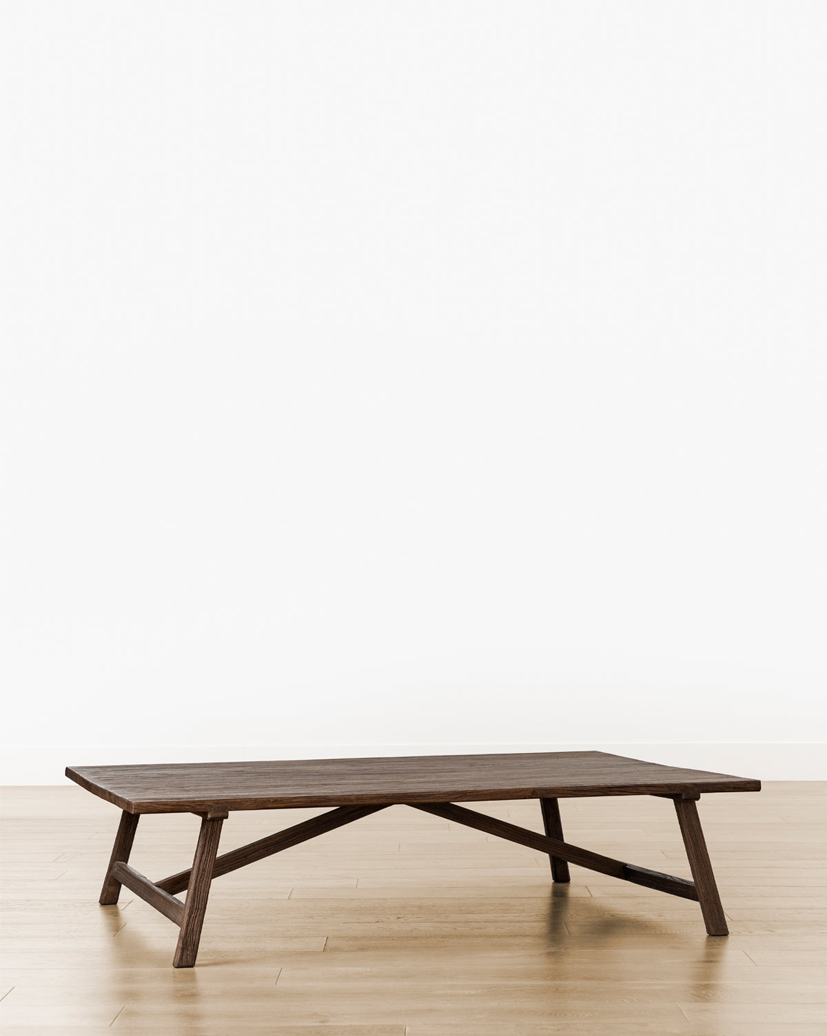 The Lockwood Coffee Table, a low rectangular piece made of English Oak with angled legs, stands on a light wood floor against a white wall, creating a minimalist and modern look, by McGee & Co.
