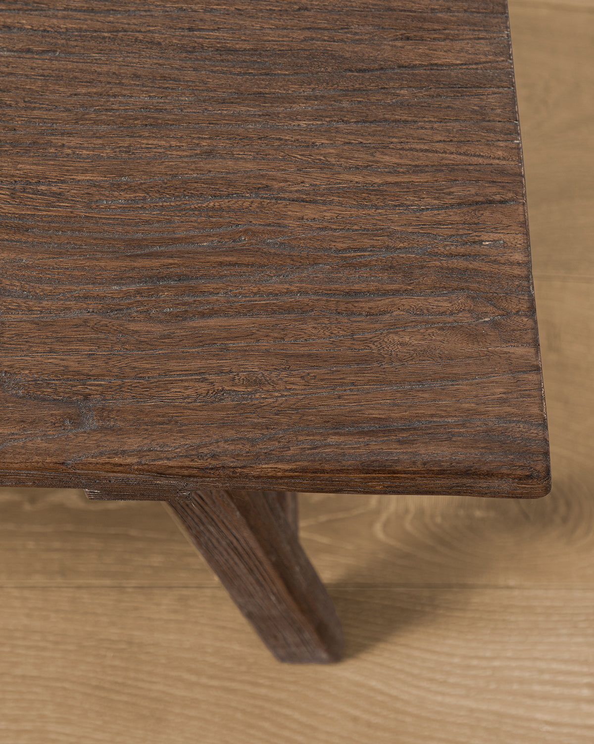 A close-up of the Lockwood Coffee Table’s corner showcases its rustic charm and rich brown finish, highlighting the wood grain detail. The table sits on a light-colored wooden floor, by McGee & Co.