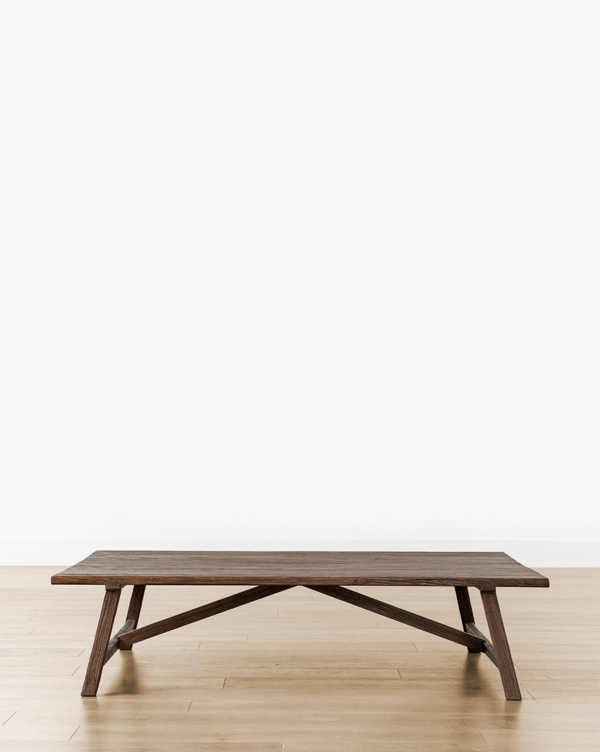 The Lockwood Coffee Table, a low rectangular piece with angled legs in English Oak, sits on a light wood floor against a plain white wall, by McGee & Co.