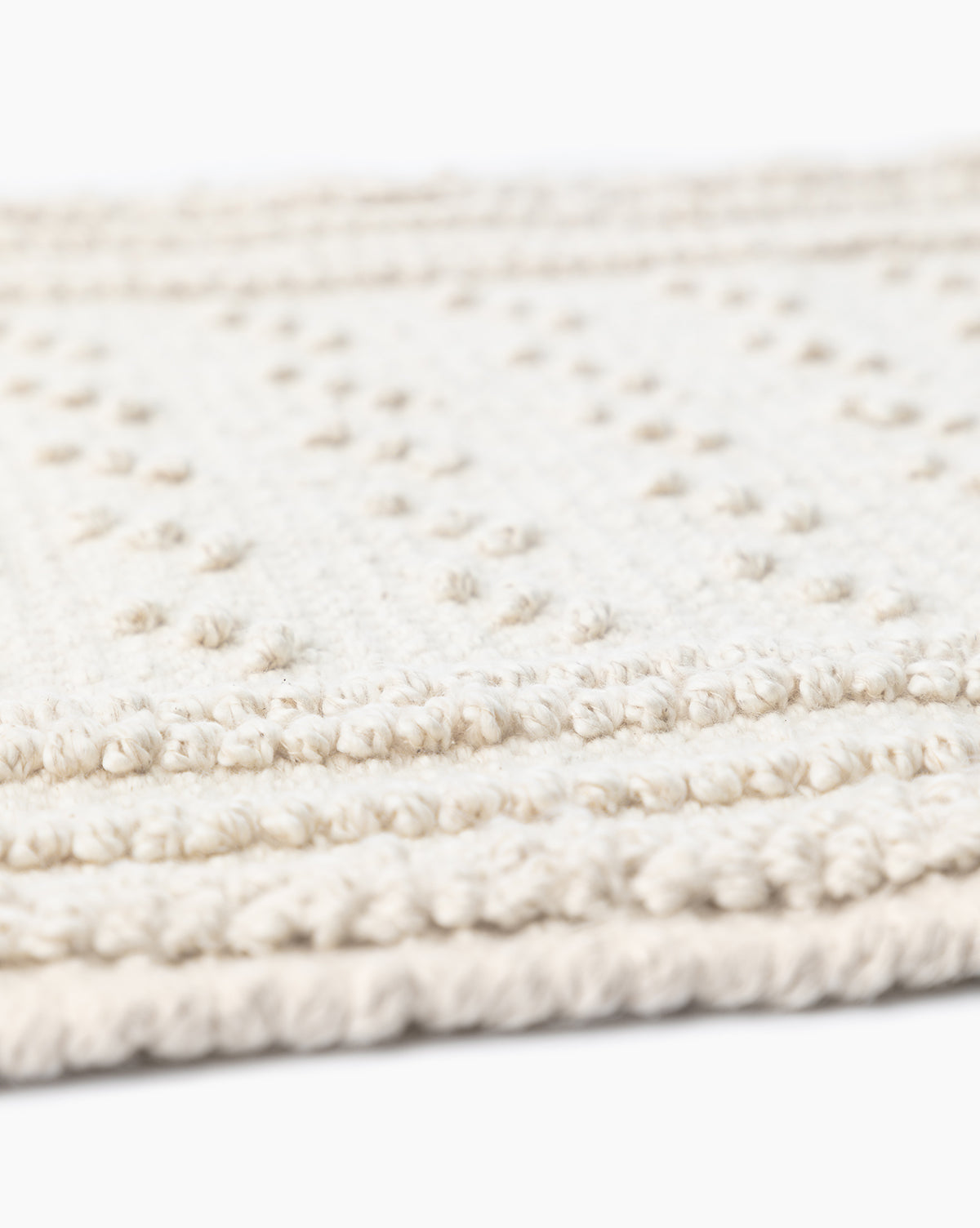 Close-up of the Lohmann Bath Mat, featuring textured off-white cotton with raised dotted patterns and stitched edges, ideal for enhancing your bathroom decor. Set against a white background.