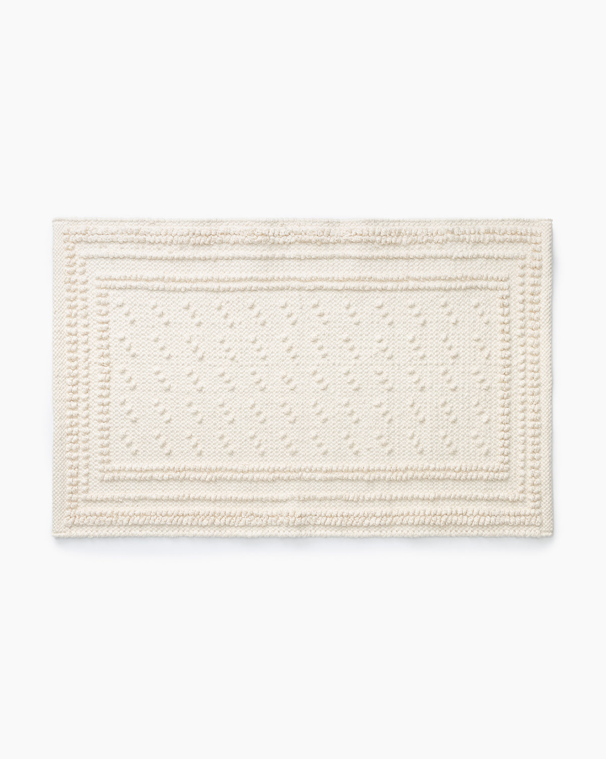 The Lohmann Bath Mat is a rectangular, off-white cotton mat with a textured finish, dotted center pattern, and raised decorative border—ideal for elevating your bathroom decor.