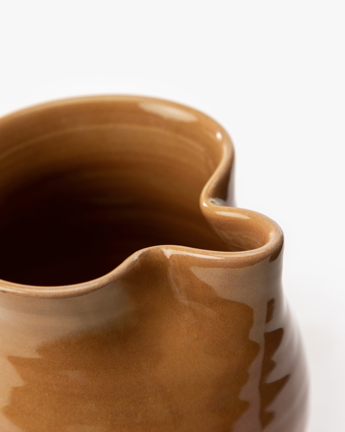 A close-up of the Louise Jug, a brown terracotta vessel with a glossy earthenware glaze, highlighting its curved rim, pouring spout, and twisted handle against a plain white background, by McGee & Co.