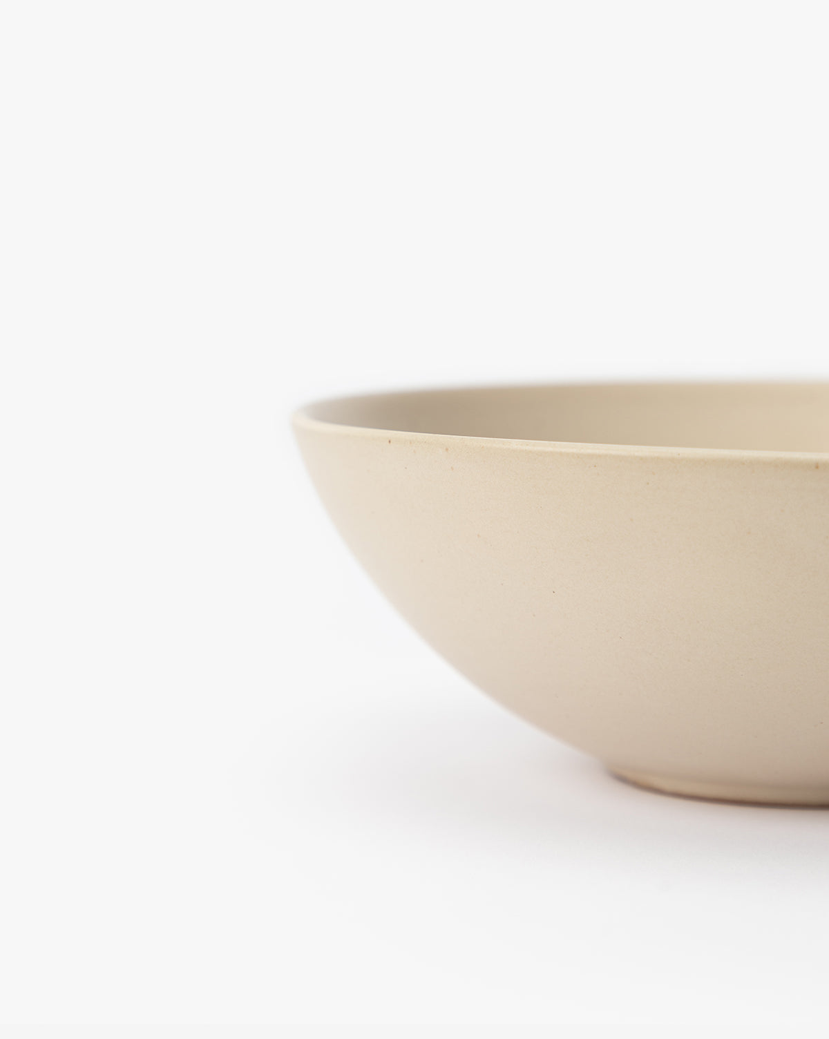 A close-up of the Luana Bowl, crafted from glazed stoneware in a modern neutral palette, showcases its smooth surface and timeless simplicity against a white background, with only part of the bowl visible on the right, by McGee & Co.