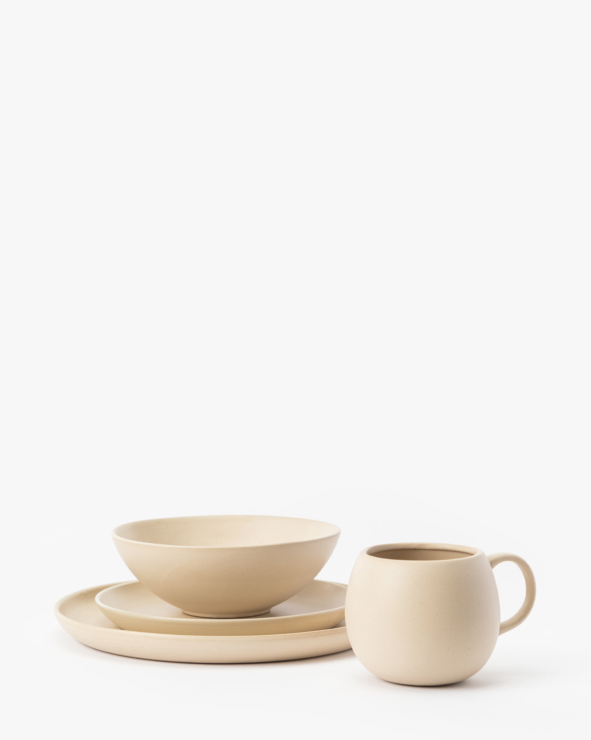 A modern beige stoneware dinnerware set featuring the Luana Bowl, a round plate, and a handled mug—all displaying a neutral palette and arranged on a white background, by McGee & Co.