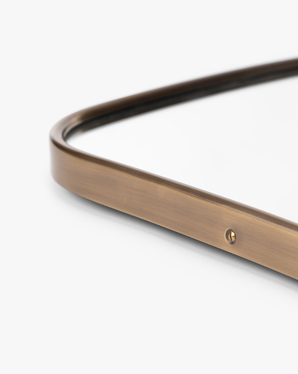 Close-up of the Ludwig Wall Mirror shows its slim metallic brass frame with a small screw detail at the edge, set against a white background, by McGee & Co.