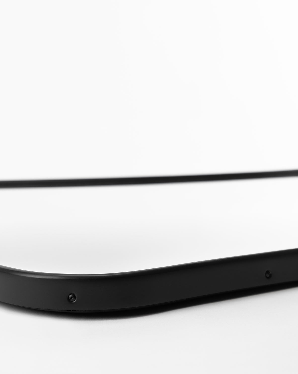 A close-up of the corner of the rectangular Ludwig Wall Mirror with a black frame, set against a white background, highlighting its smooth edge and visible screws, by McGee & Co.