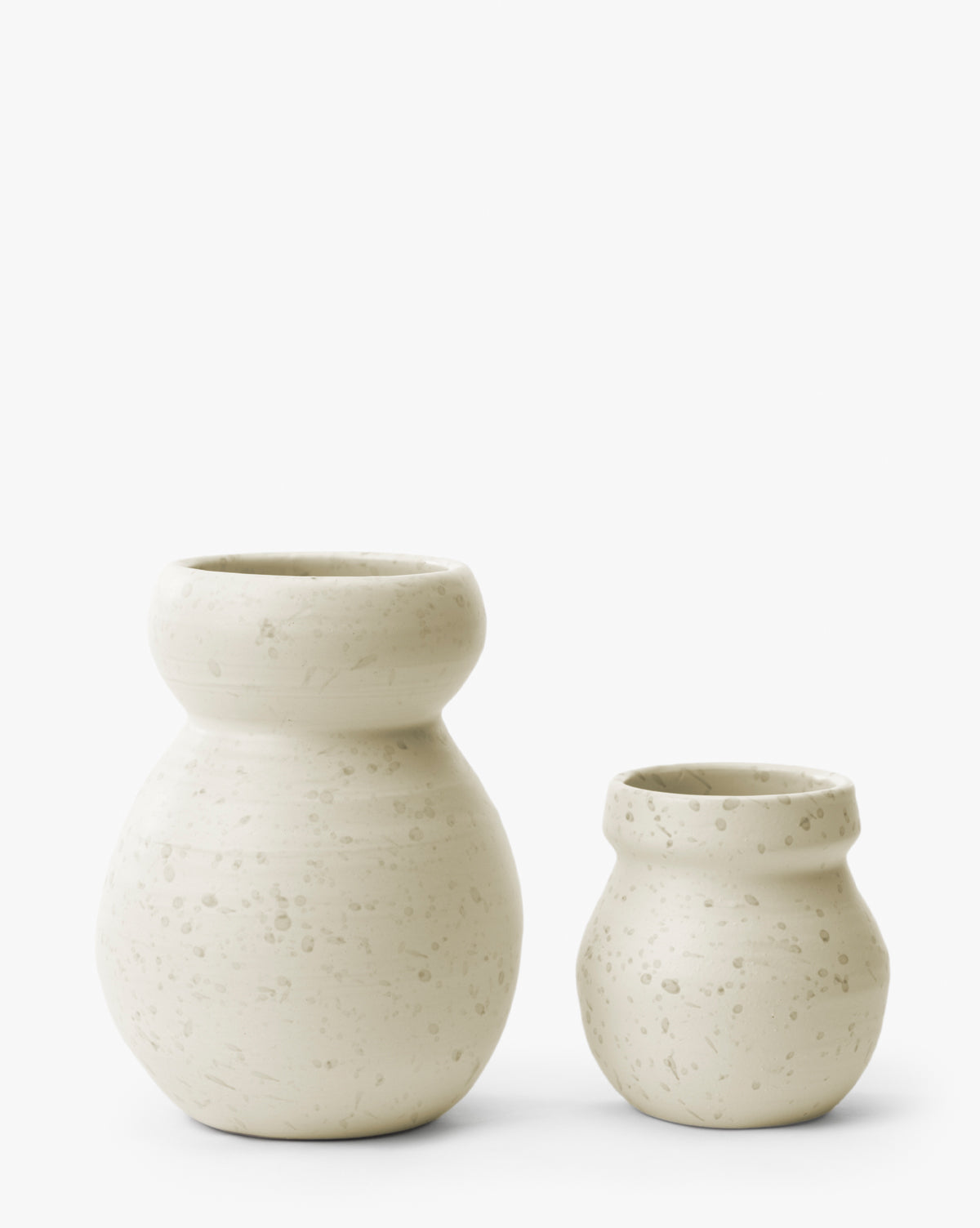 Two off-white Lyra Vases with wide necks and a subtle speckled texture are placed side by side on a plain white background. The larger white ceramic vase is on the left, and the smaller one is on the right, by McGee & Co.