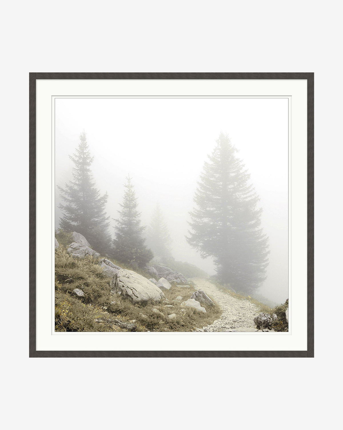 Foggy Mountain I is a giclee print of a misty forest with tall pines, rocks, and a winding path fading into fog. Set in a black woodgrain frame, this wall art features soft natural light and tranquil, muted tones.