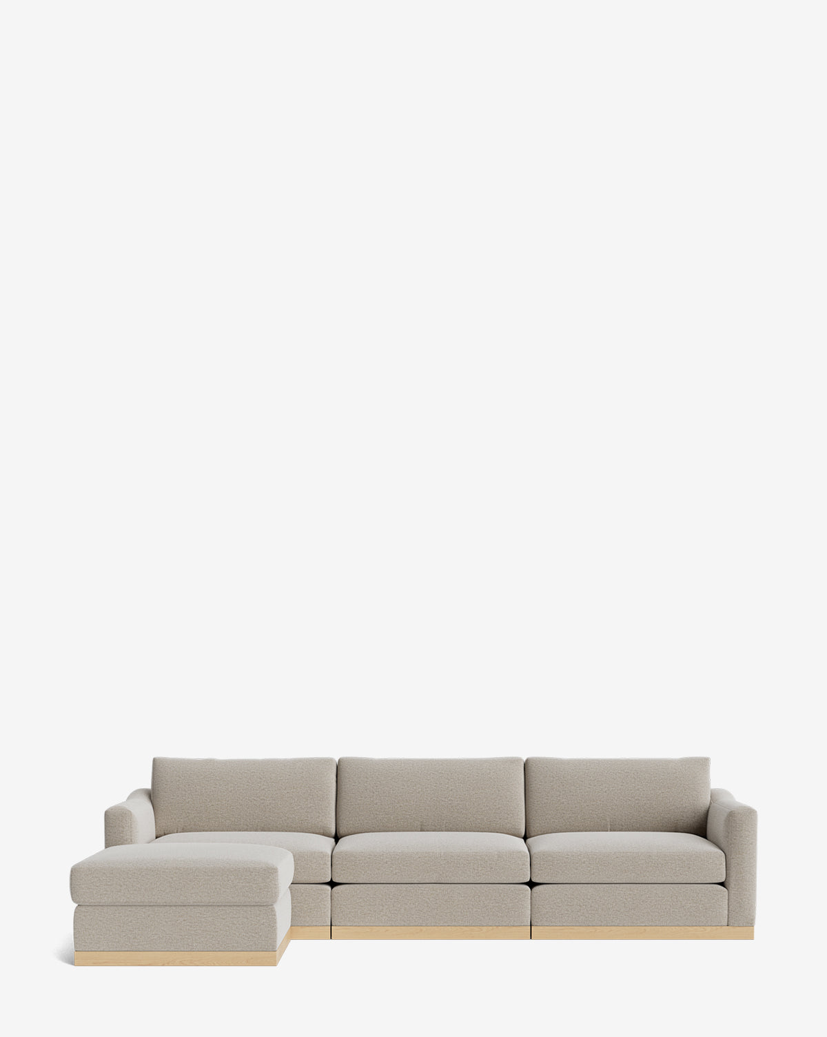 The Community Vernon Modular Sofa with Ottoman 121 is a light gray L-shaped sectional featuring customizable upholstery, a left chaise, three seat cushions, wooden base accents, and an ottoman, shown against a plain white background. McGee & Co.