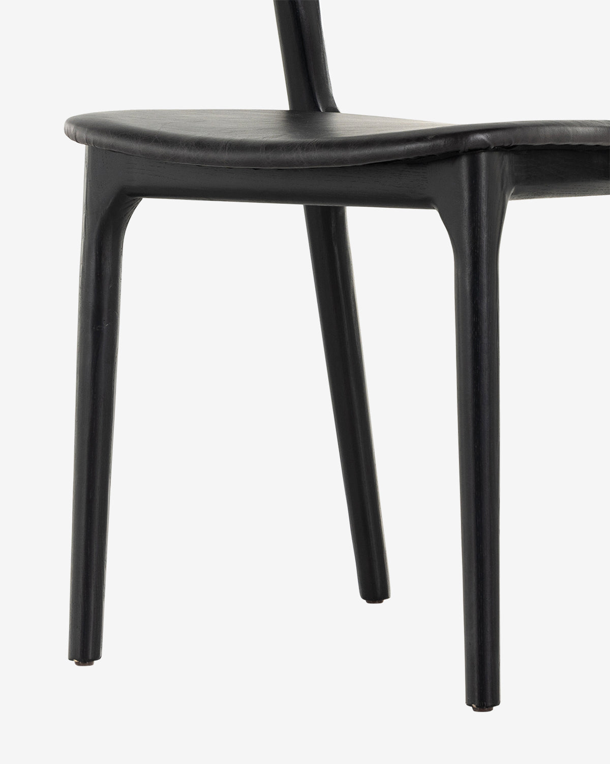 A close-up of the Lucinda Dining Chair in black, featuring sleek legs and a gently curved seat in Scandinavian style, photographed against a white background, by McGee & Co.