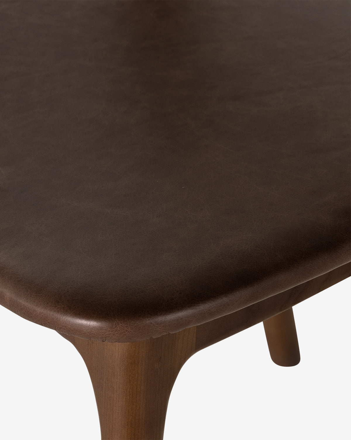 Close-up of the corner of the Lucinda Dining Chair, featuring smooth, rounded edges and a dark brown, leather-like surface. One leg is partially visible against a white background, evoking Scandinavian design, by McGee & Co.