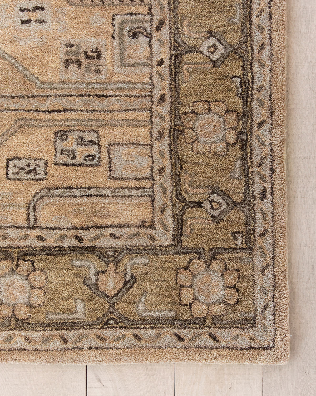 Corner of the Ellington Fawn Hand-Tufted Wool Rug, featuring beige and tan tones, intricate geometric and floral designs, a stylized floral border, and abstract rectangular motifs, shown on a light wood floor, by McGee & Co.
