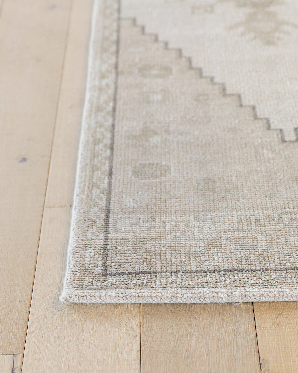 A close-up of the Pembroke Hand-Knotted Wool Rug on light wooden flooring. This beige and light gray rug features subtle geometric patterns and a thin border, bringing vintage-inspired charm to any room, by McGee & Co.