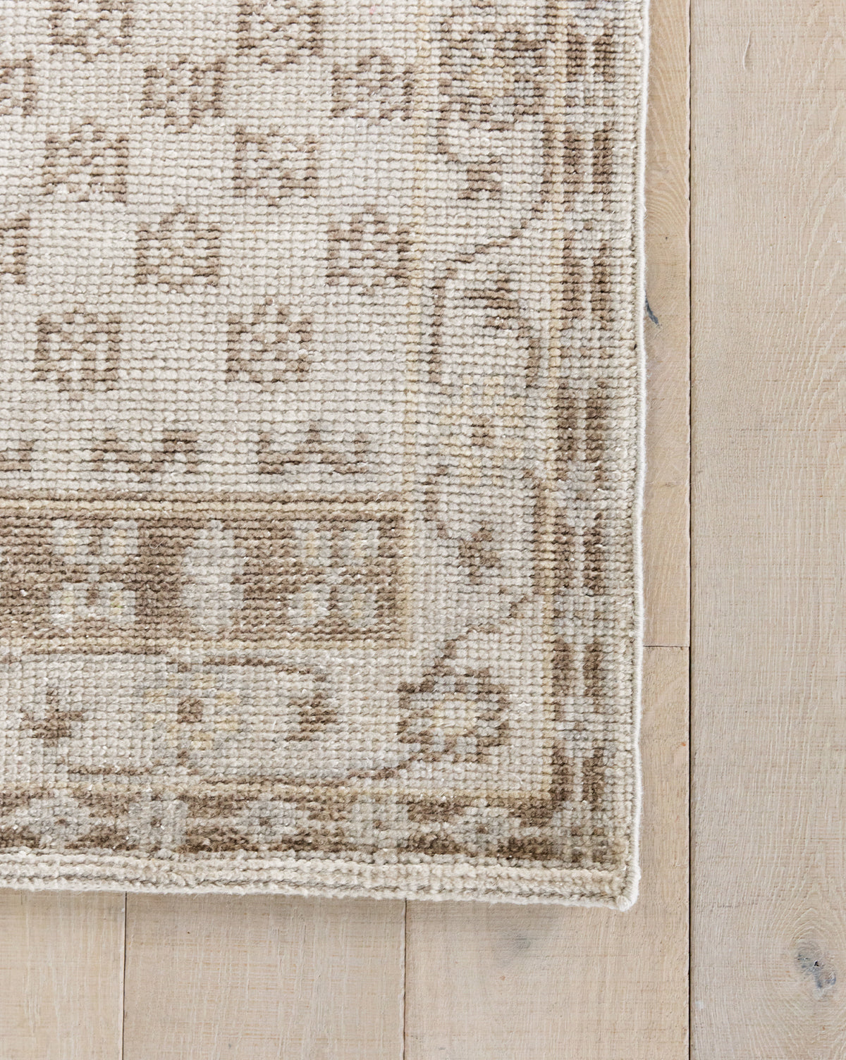 A close-up of the Anya Neutral Hand-Knotted Wool Rug on a light wood floor, showcasing its geometric and floral patterns, woven texture, and detailed edging, by McGee & Co.
