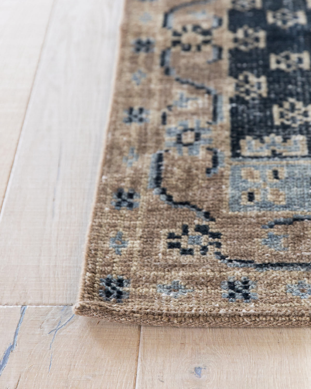 A close-up of the Anya Indigo Hand-Knotted Wool Rug shows its beige, black, and blue tones, textured weave, and transitional geometric border designs on a light wood floor, by McGee & Co.