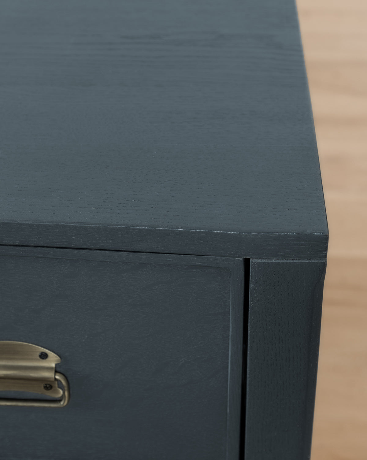 Close-up of the corner of the Mackenna Dresser in dark gray, featuring elegant brass pulls, set against a light wood floor.