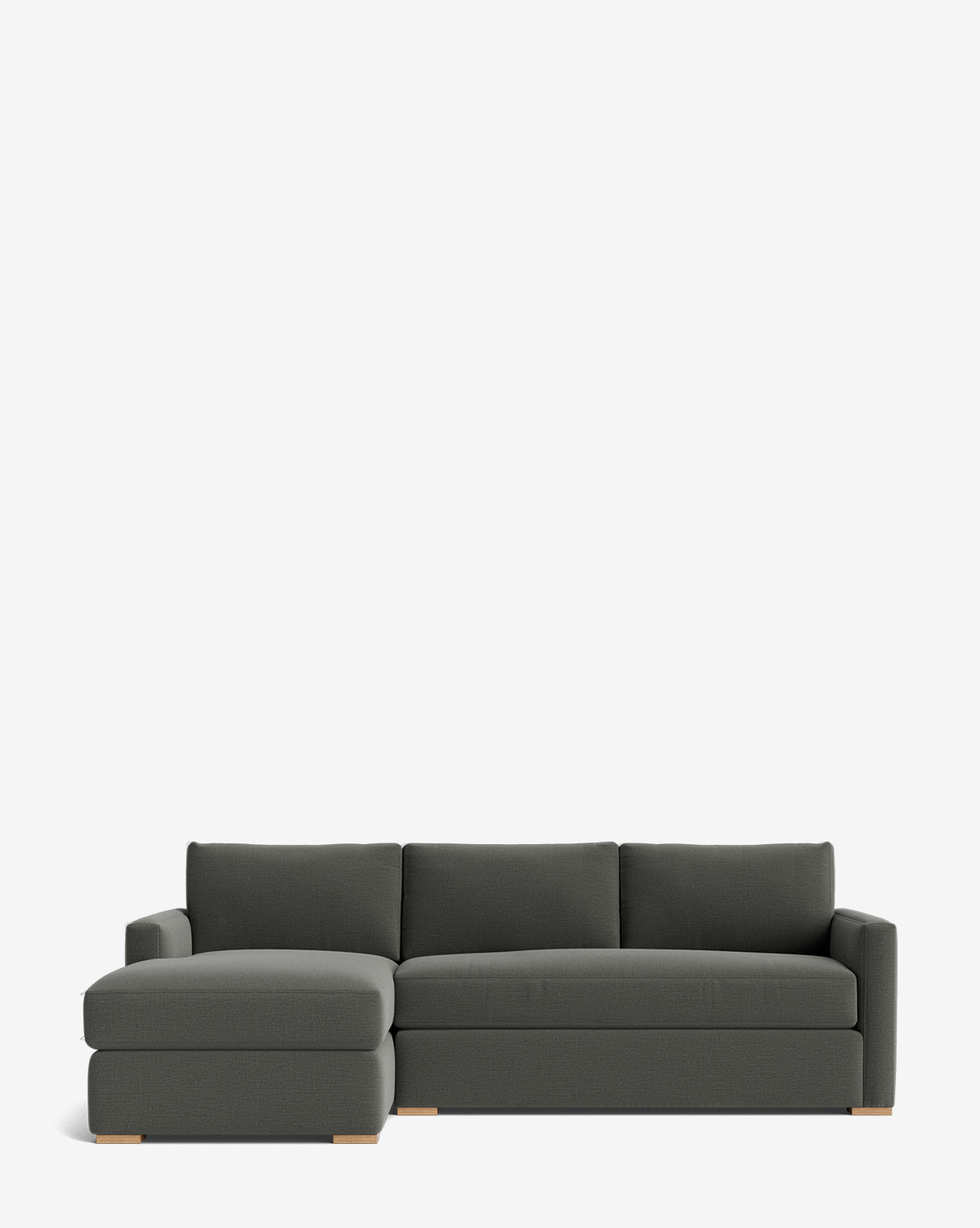 The Community Macy Upholstered Chaise Sectional 101 in dark gray features three seat and back cushions, a left-facing chaise lounge, clean lines, light wooden block legs, and a simple silhouette on a white background. McGee & Co.