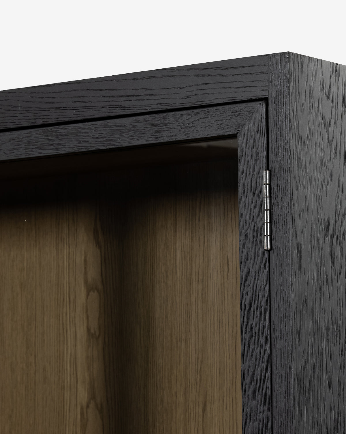 Close-up of the Maddox Bookcase door’s top corner highlights a silver hinge, lighter wood interior, and detailed oak grain—showcasing this bookcases quality construction, by McGee & Co.