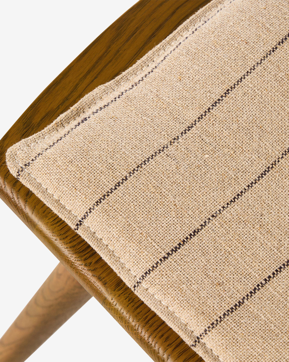 Close-up of the Madison Dining Chair with angled legs, showcasing a beige cushion with dark horizontal stripes. The textured fabric and natural wood grain highlight its contemporary Windsor style, by McGee & Co.
