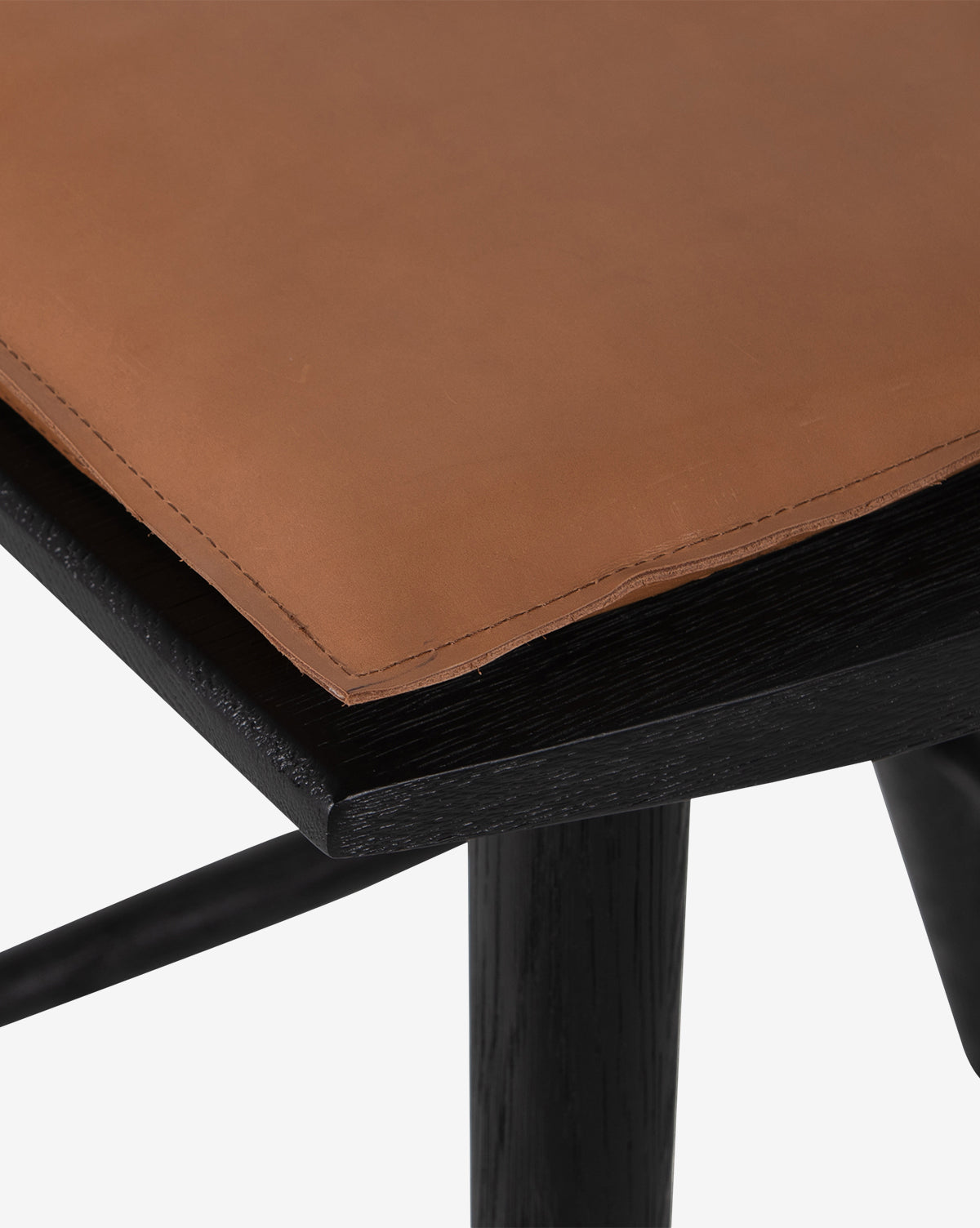 Close-up of the Madison Stools corner, featuring a brown leather seat with visible stitching and a black wooden frame—showcasing the textured materials ideal for a cushioned Windsor-style stool, by McGee & Co.