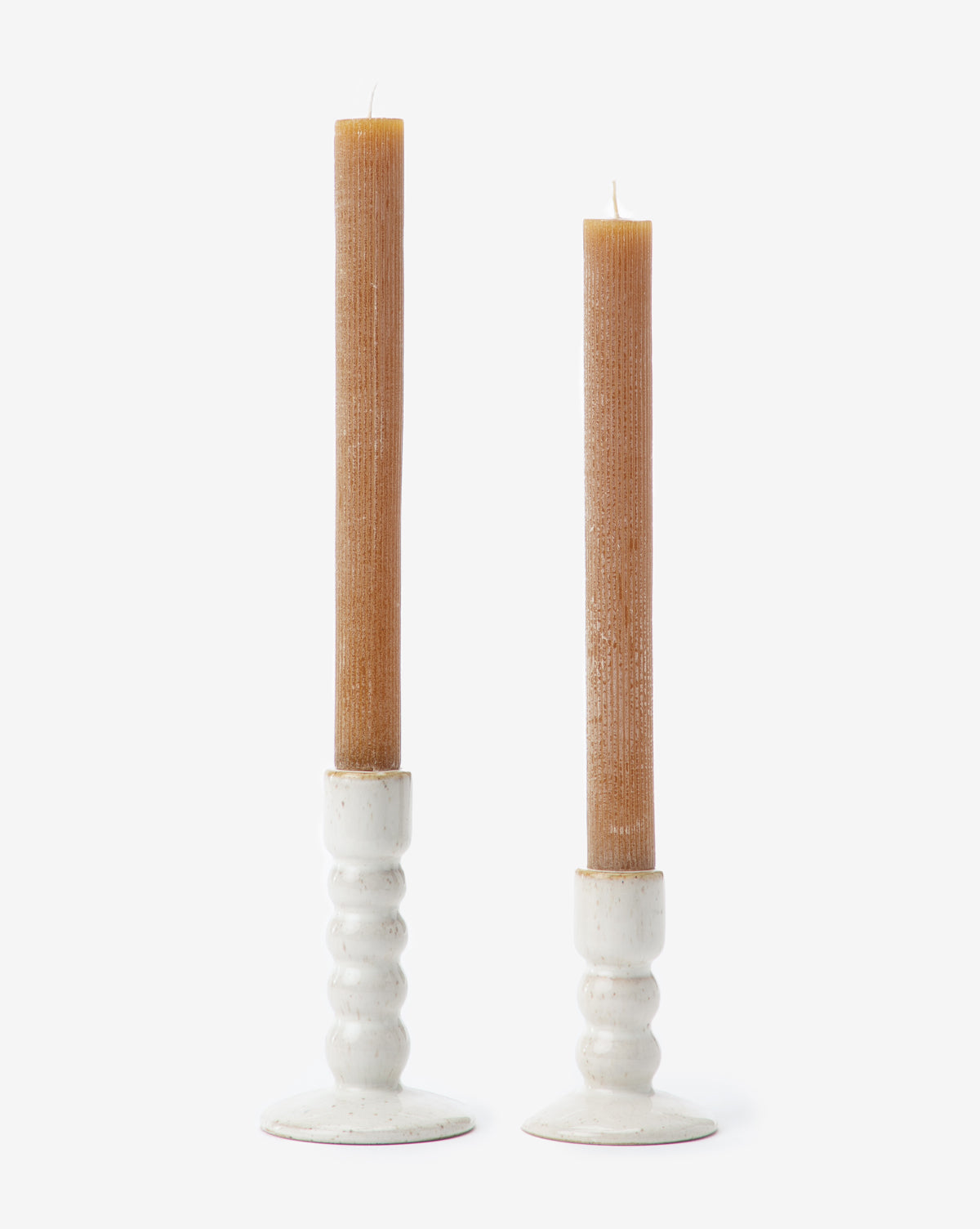 Two brown, textured taper candles rest in Mae Ceramic Taper Holders with a glossy white glaze, each holder at a different height, set against a plain white background.