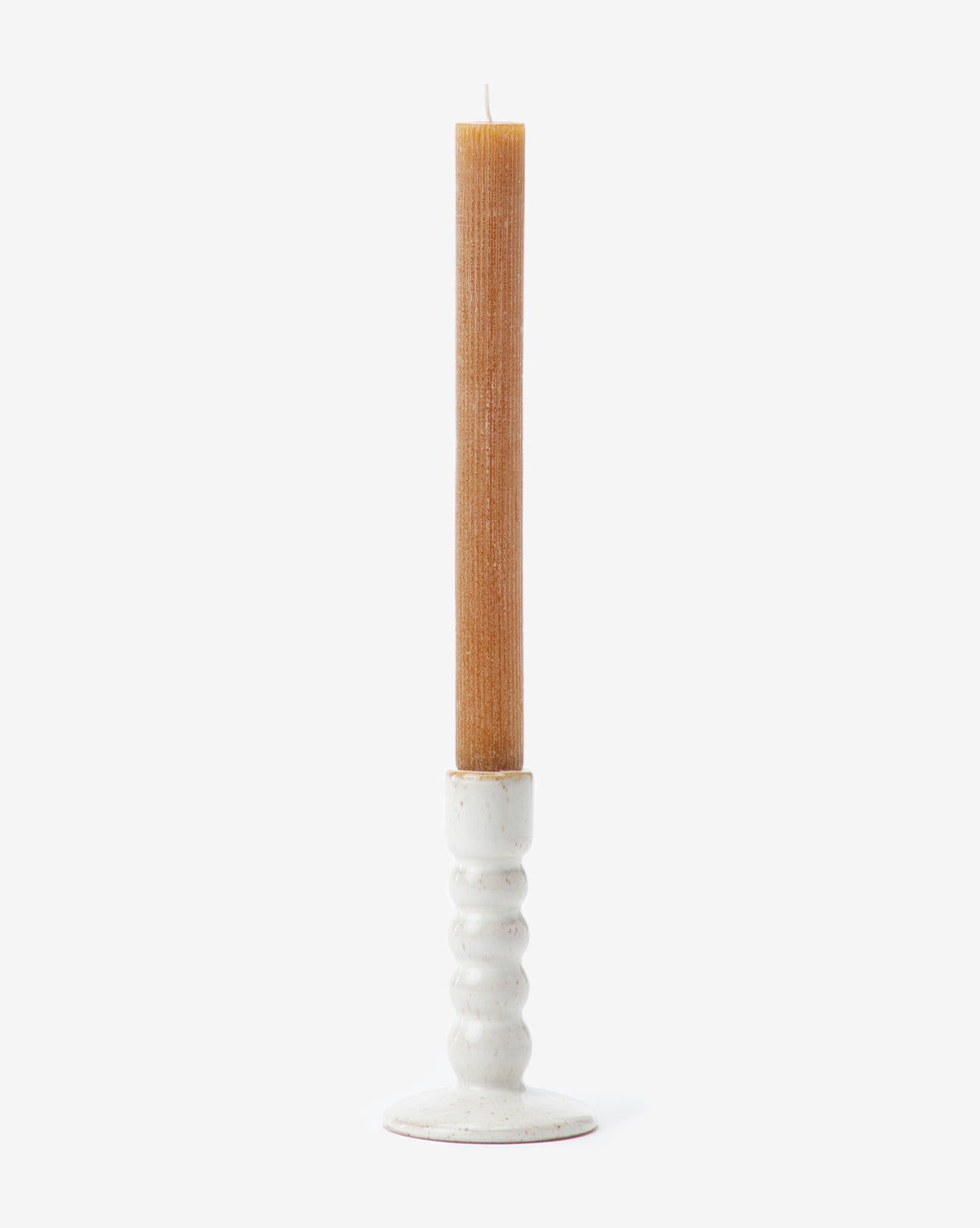 A tall brown taper candle stands upright in the Mae Ceramic Taper Holder, which features a rounded, textured base and glossy white glaze, set against a plain white background.
