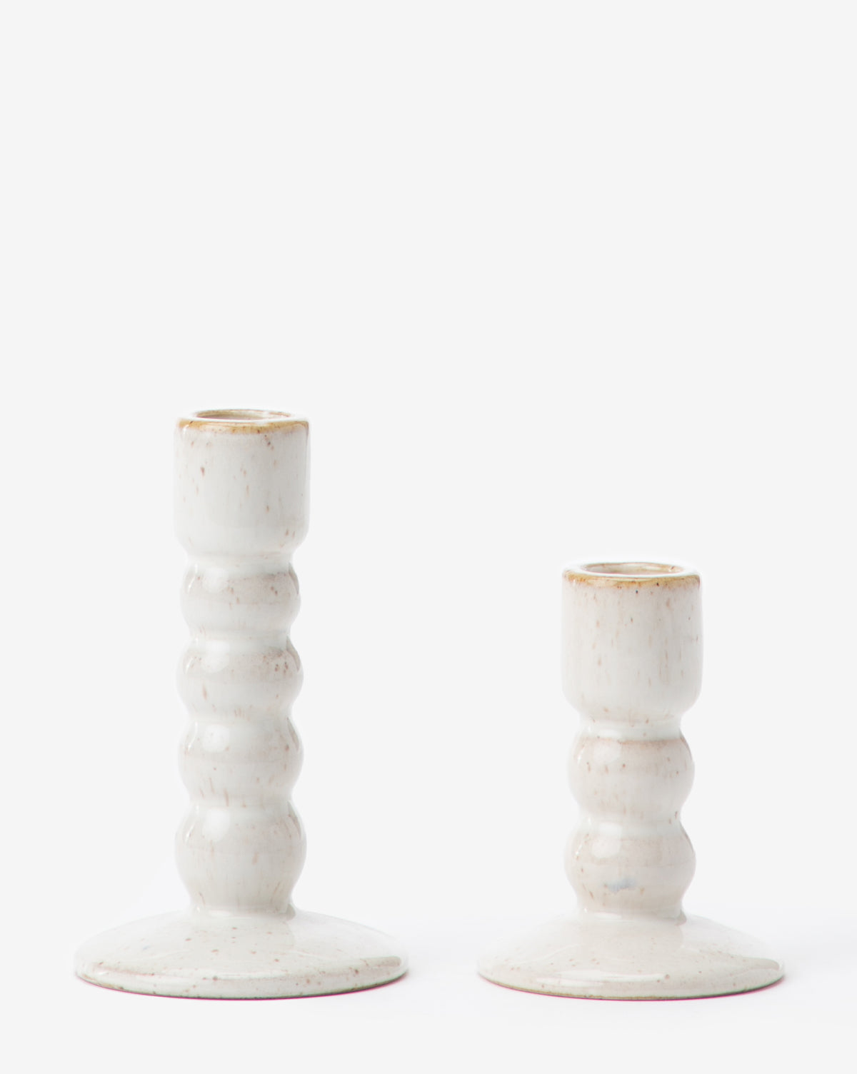 The Mae Ceramic Taper Holder set features two white stoneware holders with speckled glaze and ribbed stems—one taller than the other. Both have wide, flat bases and add an elegant touch to any décor.