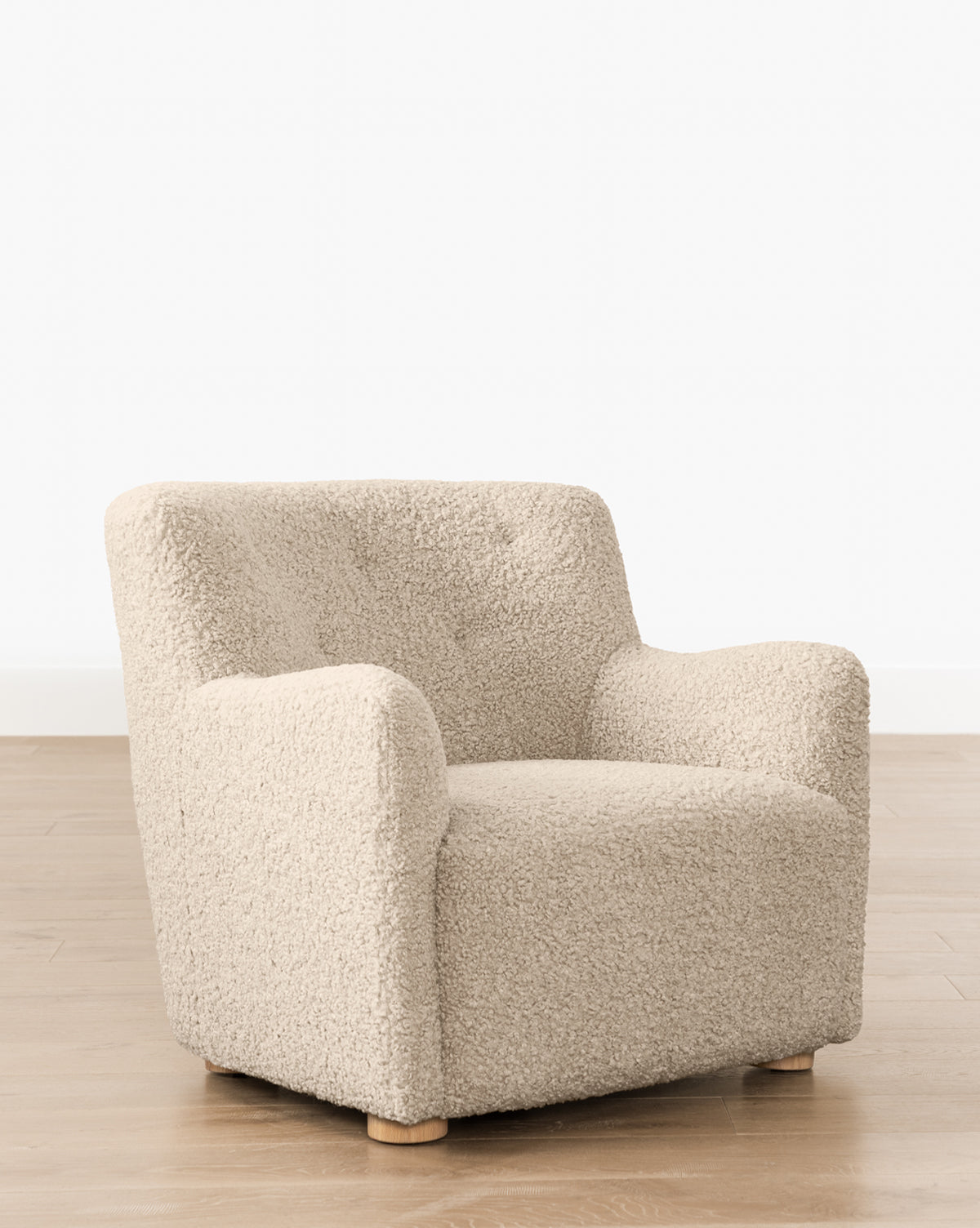 The Magda Lounge Chair (Ready to Ship) features plush, textured beige fabric, rounded arms, and short wooden legs. Its modern design adds a stylish touch when placed on a light wood floor against a white wall, by McGee & Co.