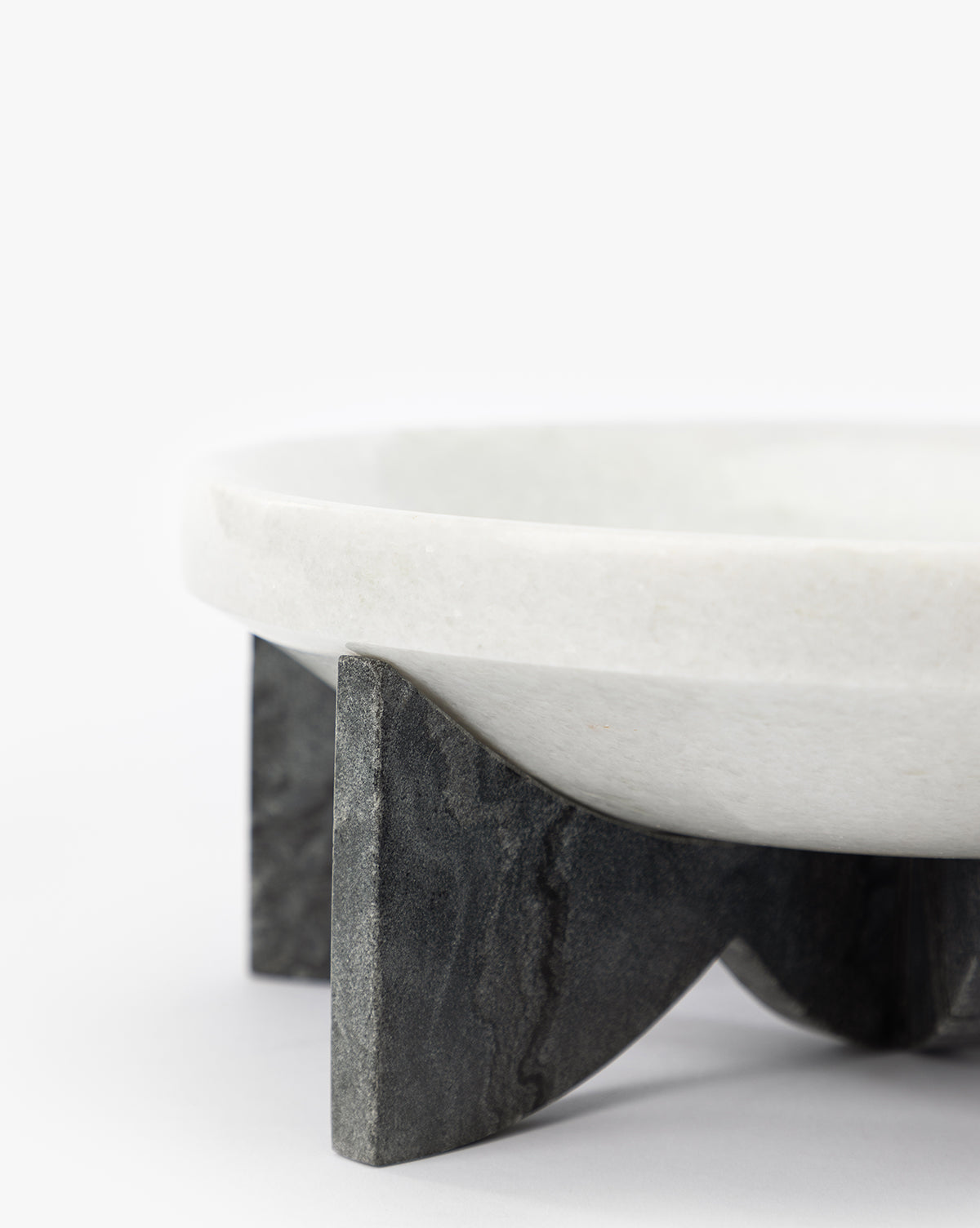 The Mahoney Bowl, featuring a sculptural white marble form, is displayed on a dark three-legged stone stand against a plain white background, by McGee & Co.