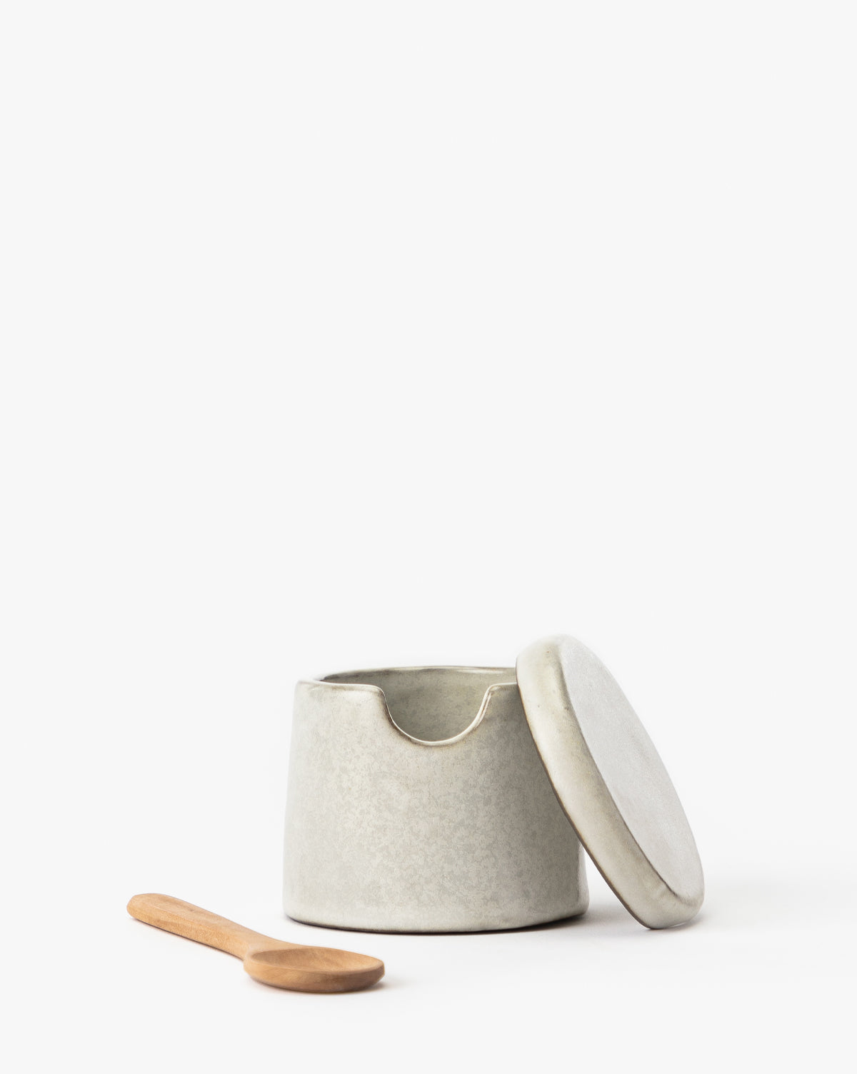 The Malco Salt Cellar, made of ceramic and featuring a rim notch, is displayed with its lid angled beside it and a wooden spoon in front, all set against a plain white background.