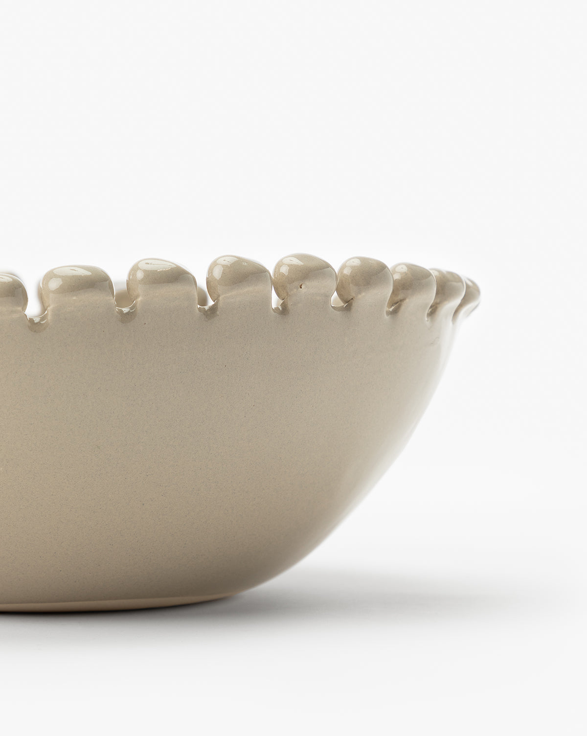 A close-up of the Malibu Bowl, a beige ceramic piece with a scalloped, rounded rim, is shown against a white background. Only part of this unique kitchen décor item is visible in the image, by McGee & Co.