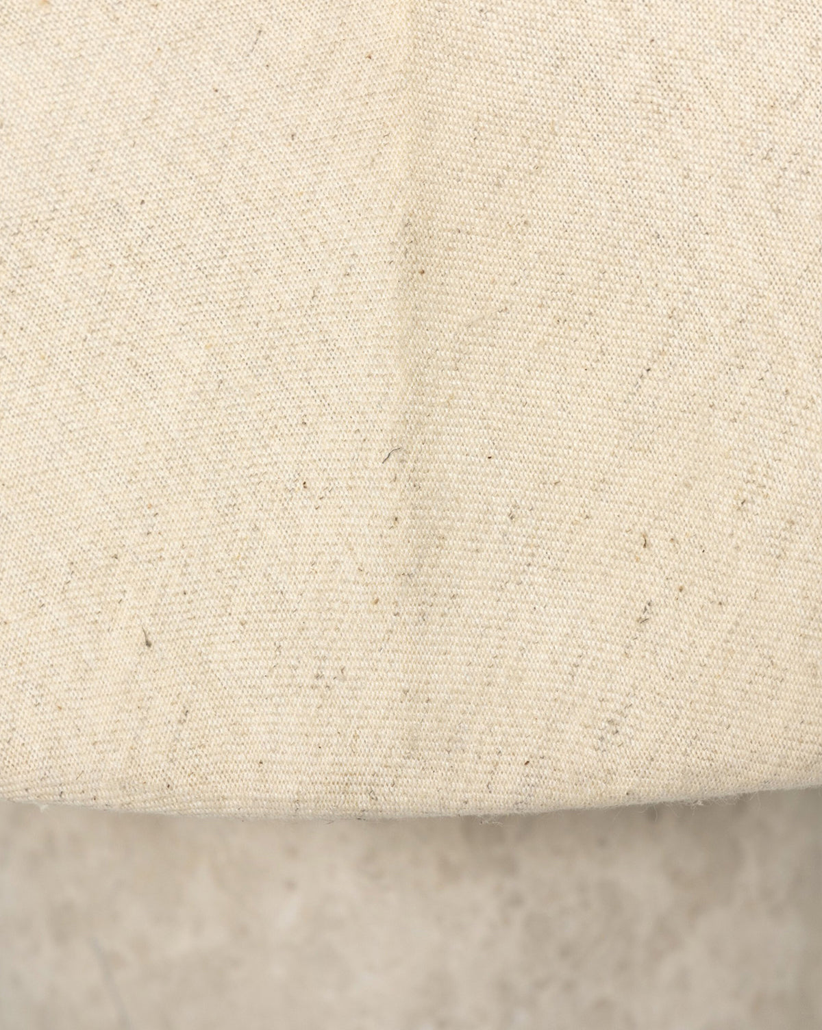 Close-up of the Malinska Table Lamps beige linen dome shade, featuring a visible center seam, coarse texture with scattered dark fibers, and a curved edge that reveals its gray concrete base, by McGee & Co.