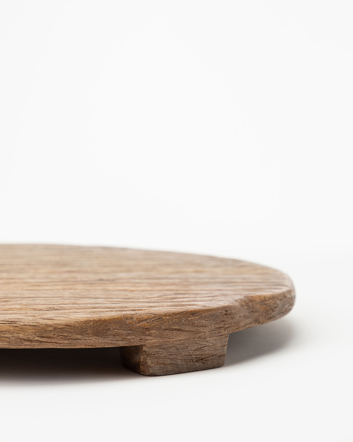 A close-up of the Mango Wood Carved Pedestal, an elevated round serving tray with short legs on a white background, highlighting its textured natural wood grain and color.