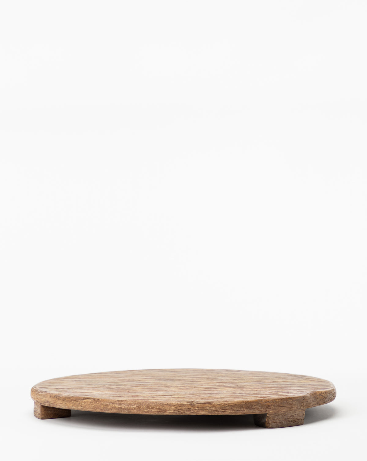 The Mango Wood Carved Pedestal is a round, flat serving board with short legs that offers an elegant, elevated display against a white background.