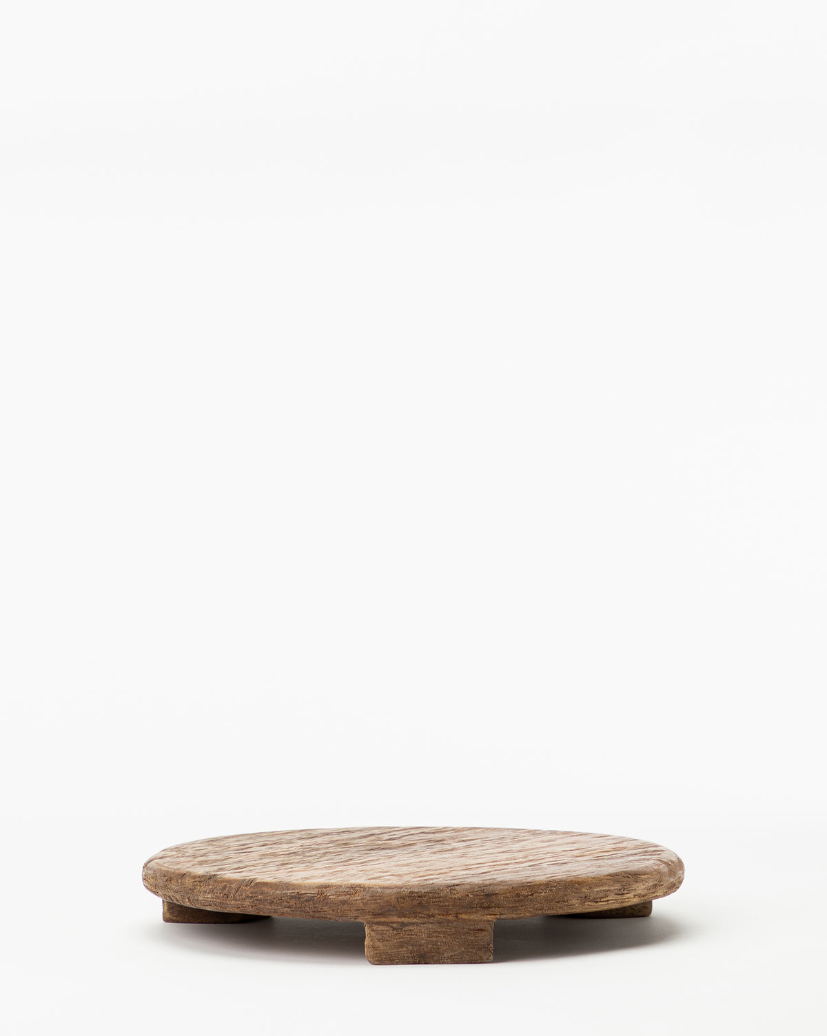 The Mango Wood Carved Pedestal features a small, round design with a textured surface and short block legs, making it ideal as an elevated serving tray. Shown on a plain white background.