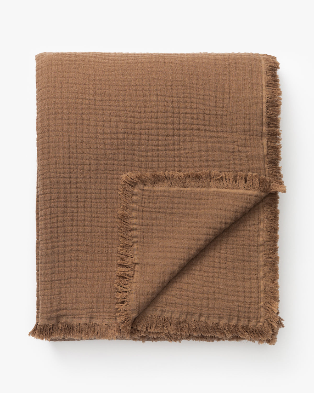 The Marinella Oversized Waffle Throw, shown folded on a white background, features a rich brown color, textured cotton in a waffle weave, and fringed edges. One corner is turned up to highlight its thickness and texture.