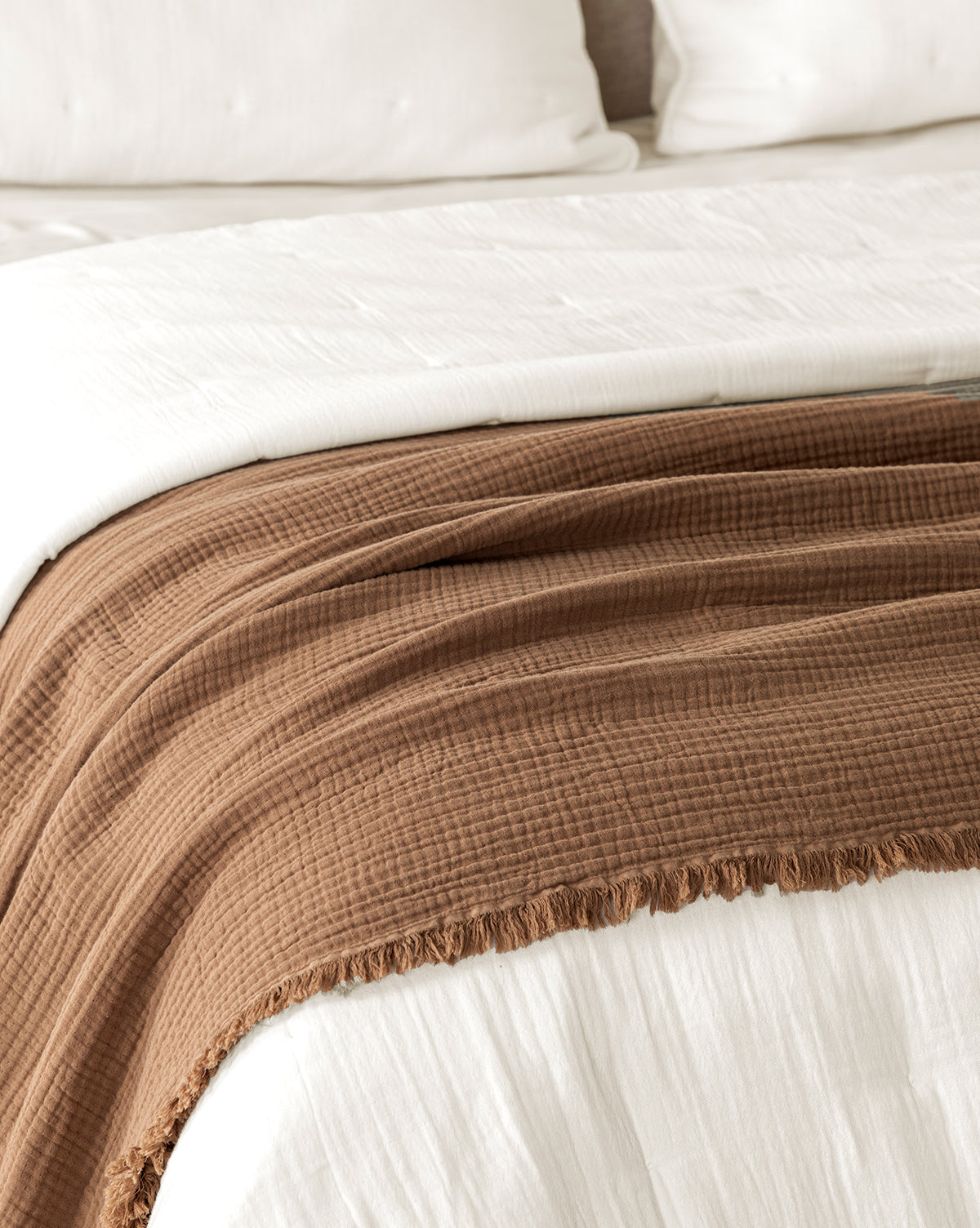 A neatly made bed with white bedding and pillows is topped with the Marinella Oversized Waffle Throw, featuring a textured waffle weave and fringed edges that add warmth and style at the foot of the bed.