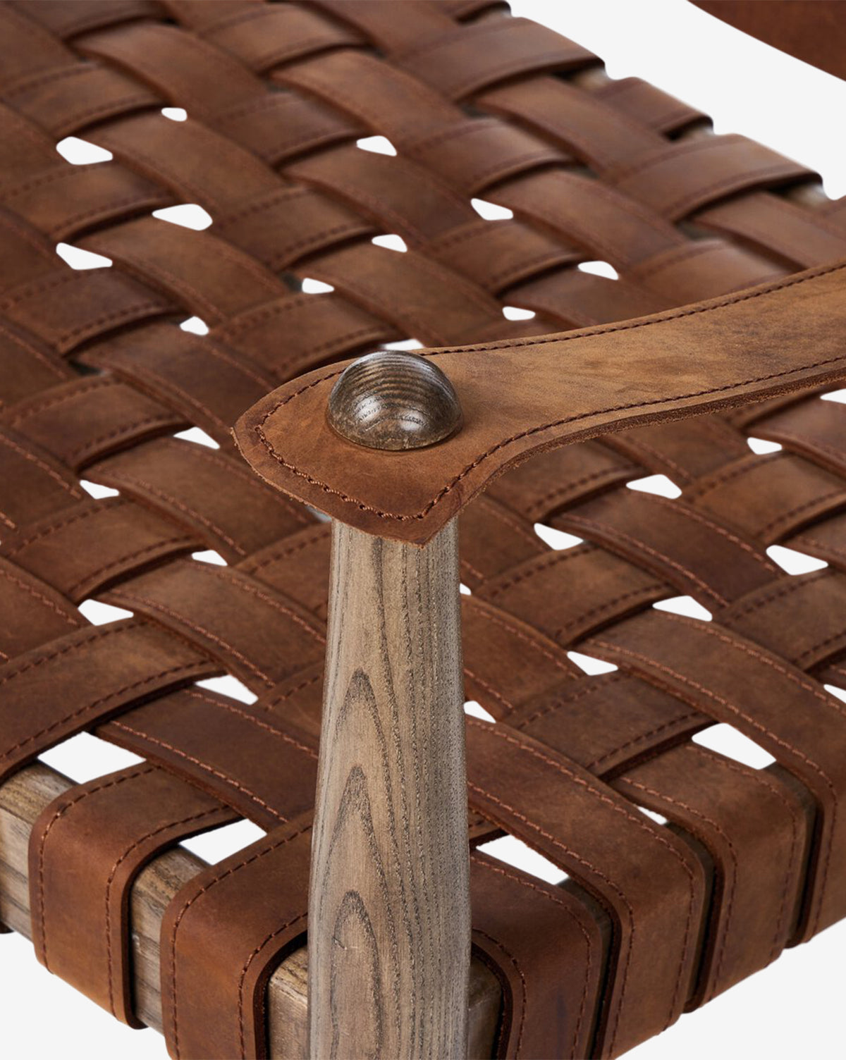 Close-up of the Maris Lounge Chair, highlighting its vintage-inspired woven brown leather seat and back, light wood armrests and frame, with the armrest joined by a round wooden peg, by McGee & Co.